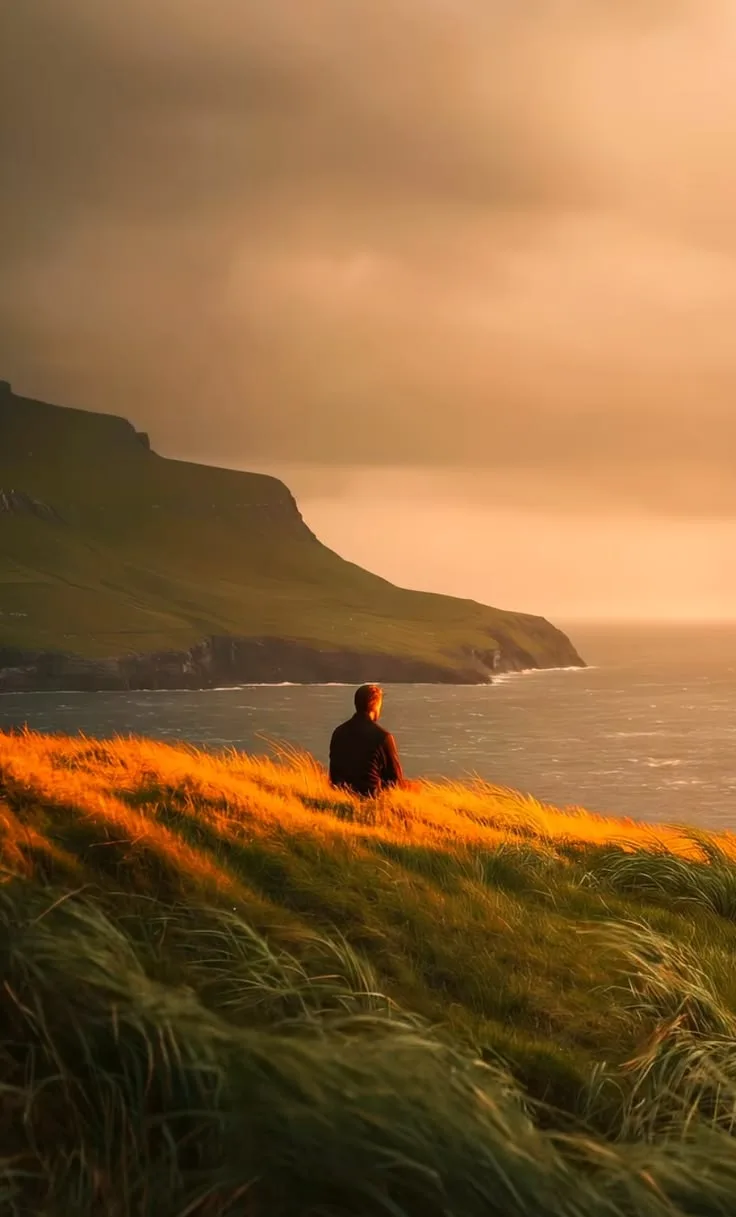 A lone figure on a grassy headland above the sea at dusk